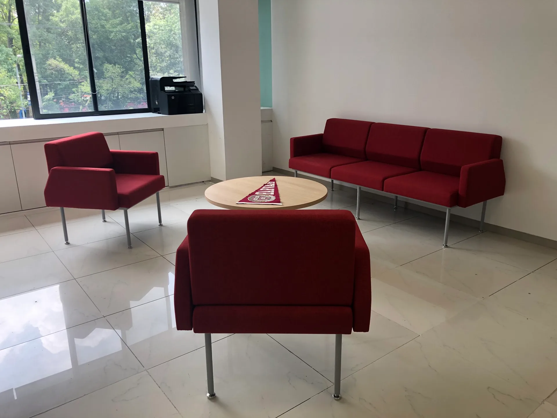 Sala de espera de Harvard con sofá y sillones rojos alrededor de mesa redonda, por Poliarte