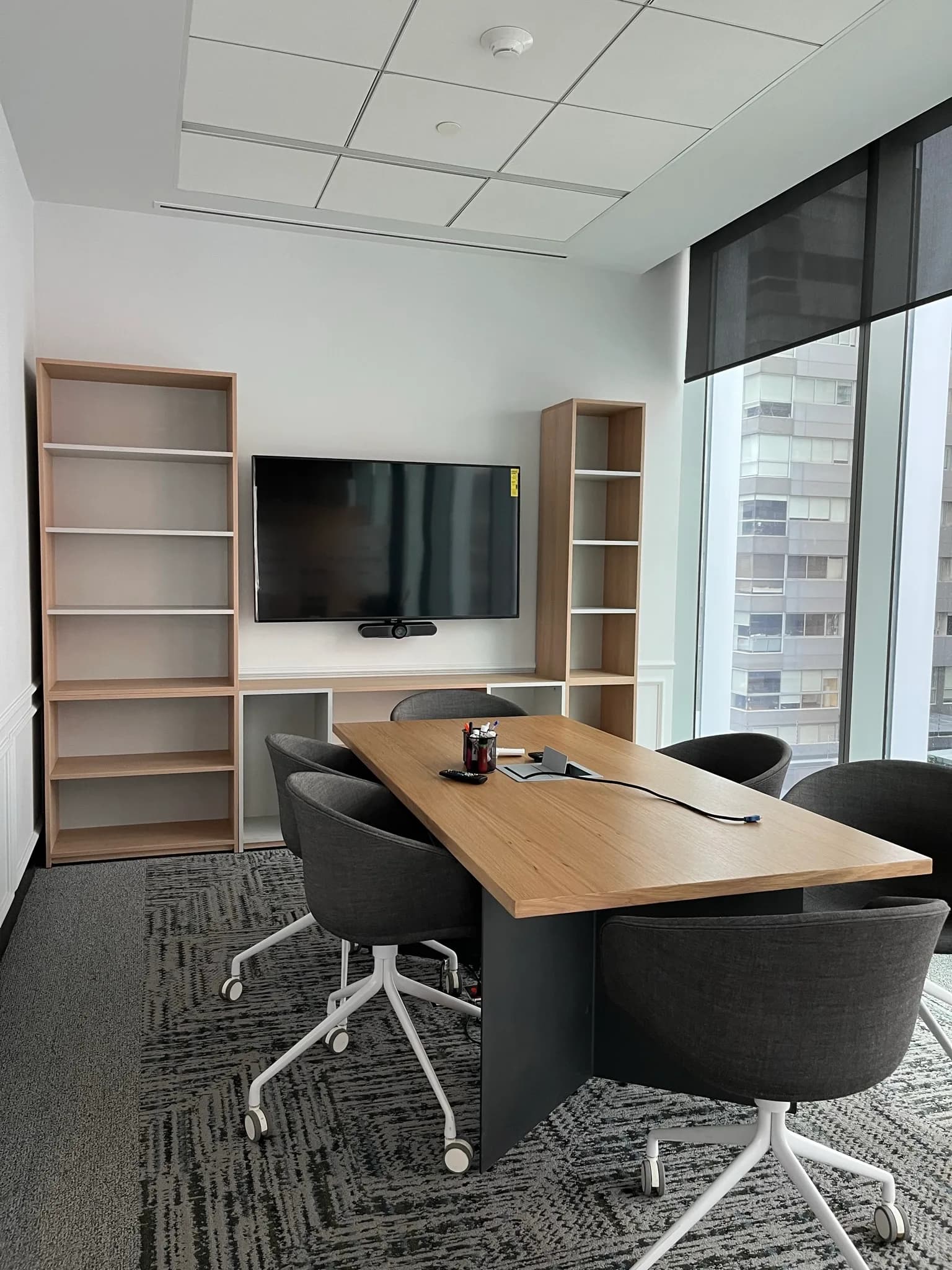 Sala de juntas de Harvard con mesa de madera, sillas grises y libreros con pantalla, por Poliarte