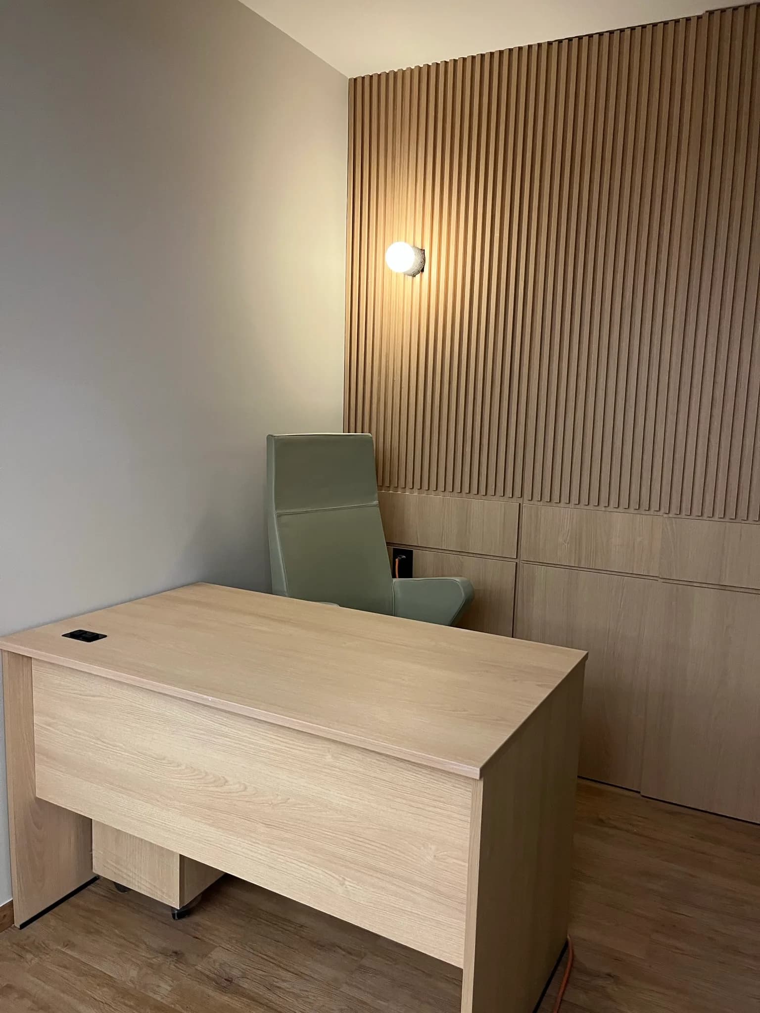 Privado de Capdeville con escritorio de madera clara, silla ejecutiva verde y muro de lambrín, por Poliarte