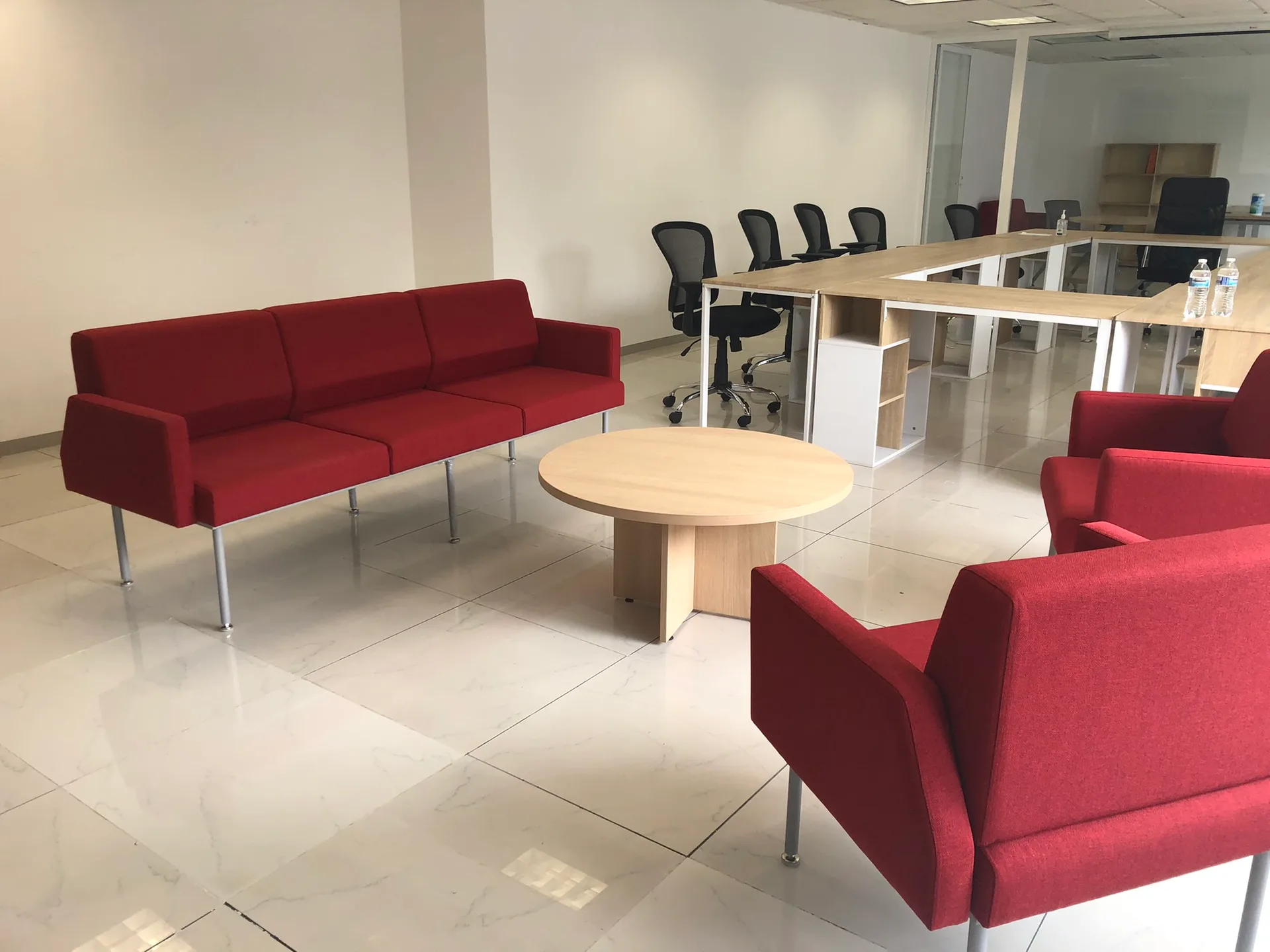 Sala de espera de Harvard con sofás rojos, mesa de centro redonda y estaciones al fondo, por Poliarte