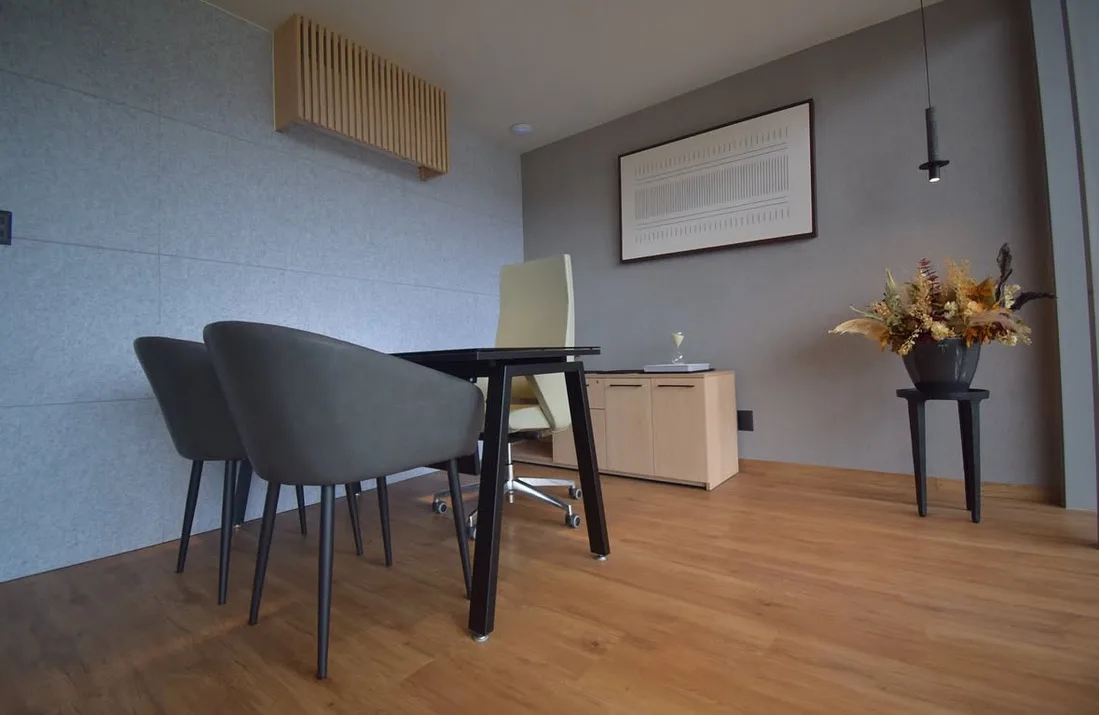 Privado de Capdeville con escritorio de patas negras, credenza clara y dos sillones grises, por Poliarte