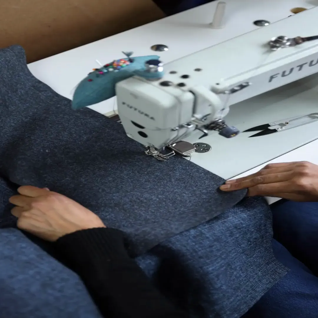 Manos guiando una tela azul en la máquina de coser del taller de tapicería de Poliarte