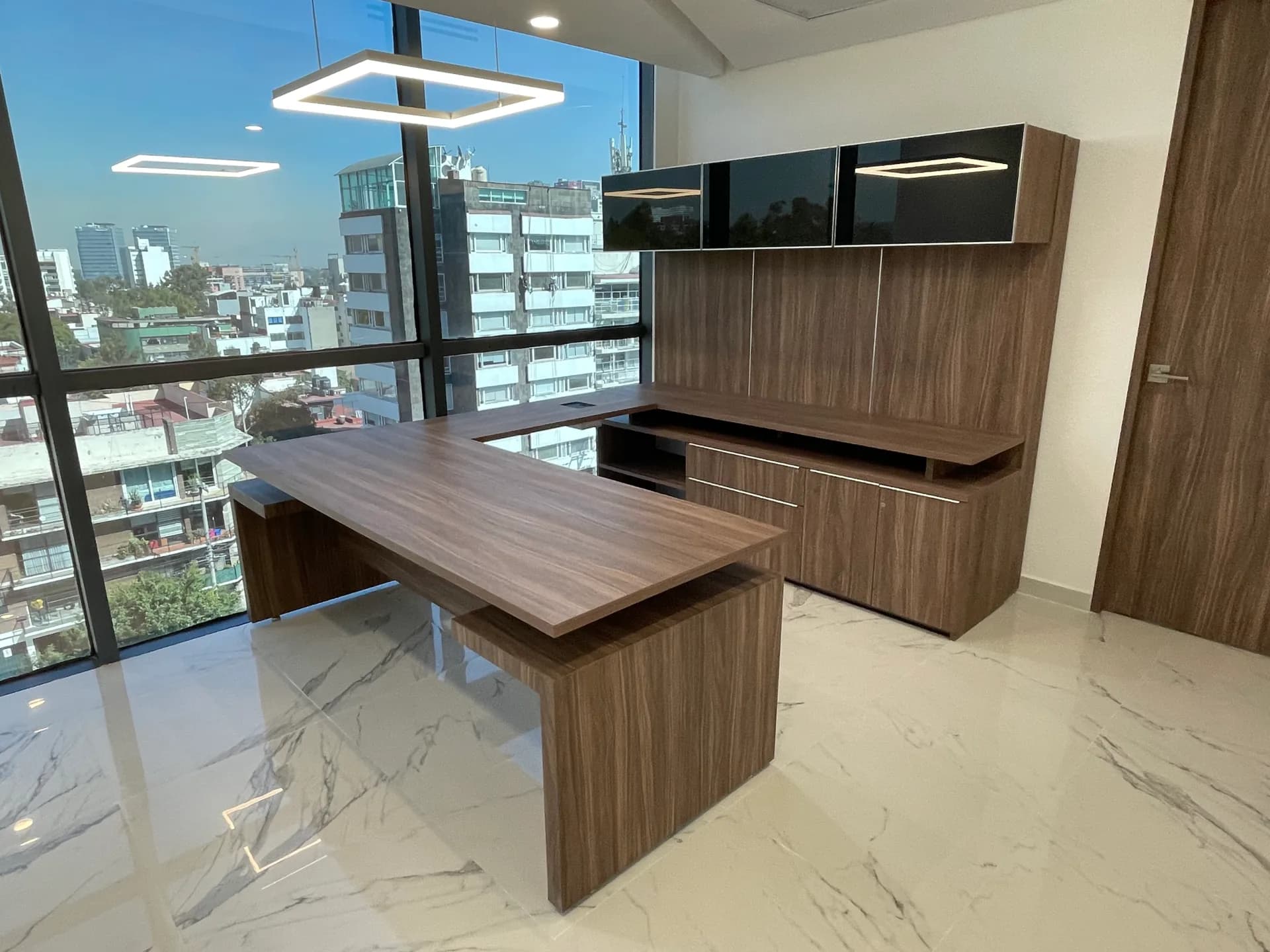 Privado de Cayeno con escritorio nogal de paneles, credenza y gabinetes altos junto al ventanal, por Poliarte