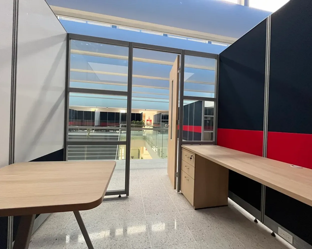 Cubículo de La Salle con muros divisorios azul y rojo, cubierta de madera y cajonera, por Poliarte