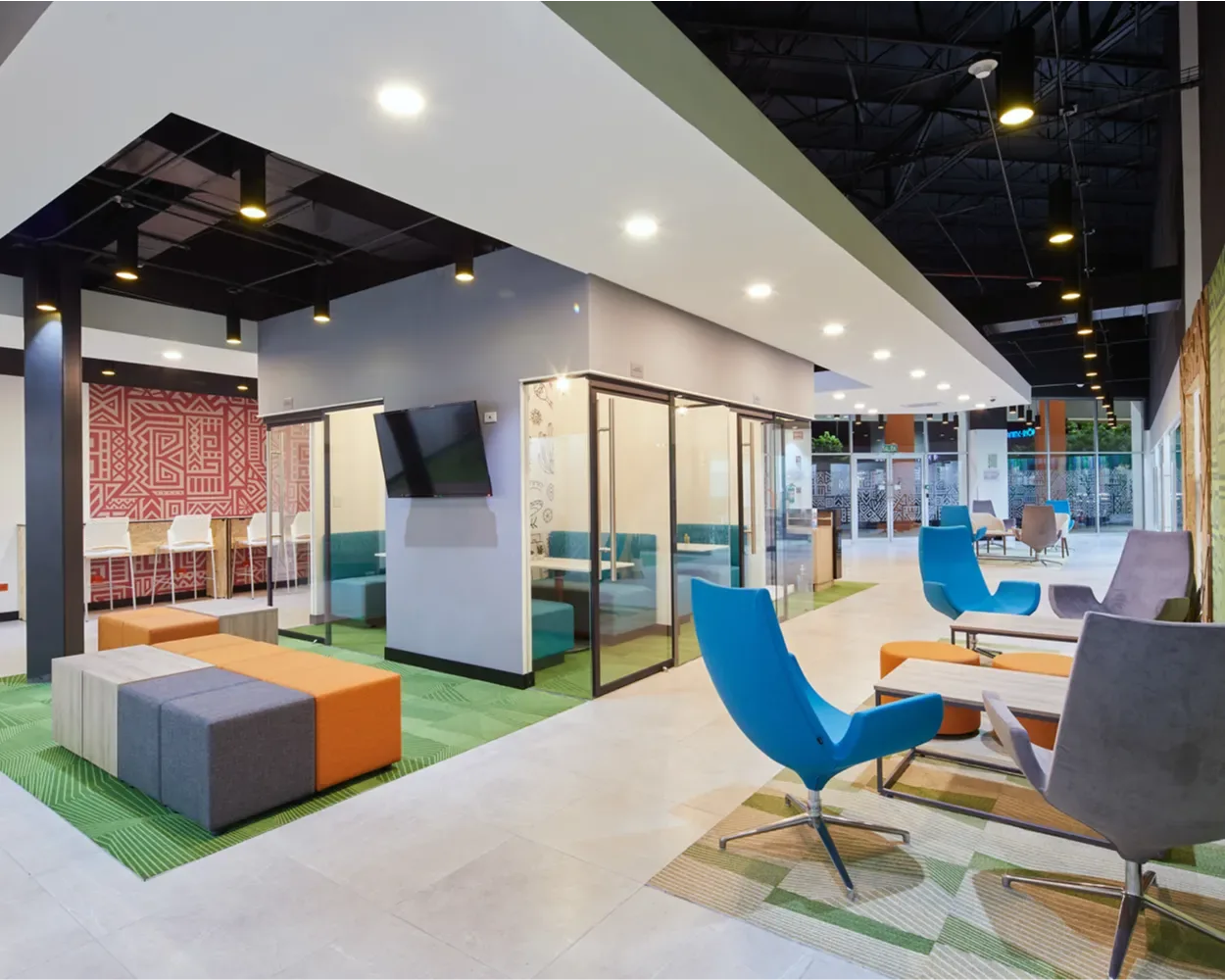 Área lounge de Newcore Industries con sillones azules y grises y puffs de colores, mobiliario de Poliarte