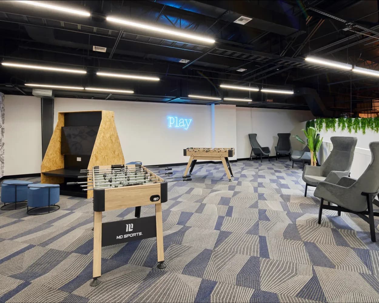 Área de juegos de Newcore Industries con futbolito, sillones grises de respaldo alto y puffs, por Poliarte