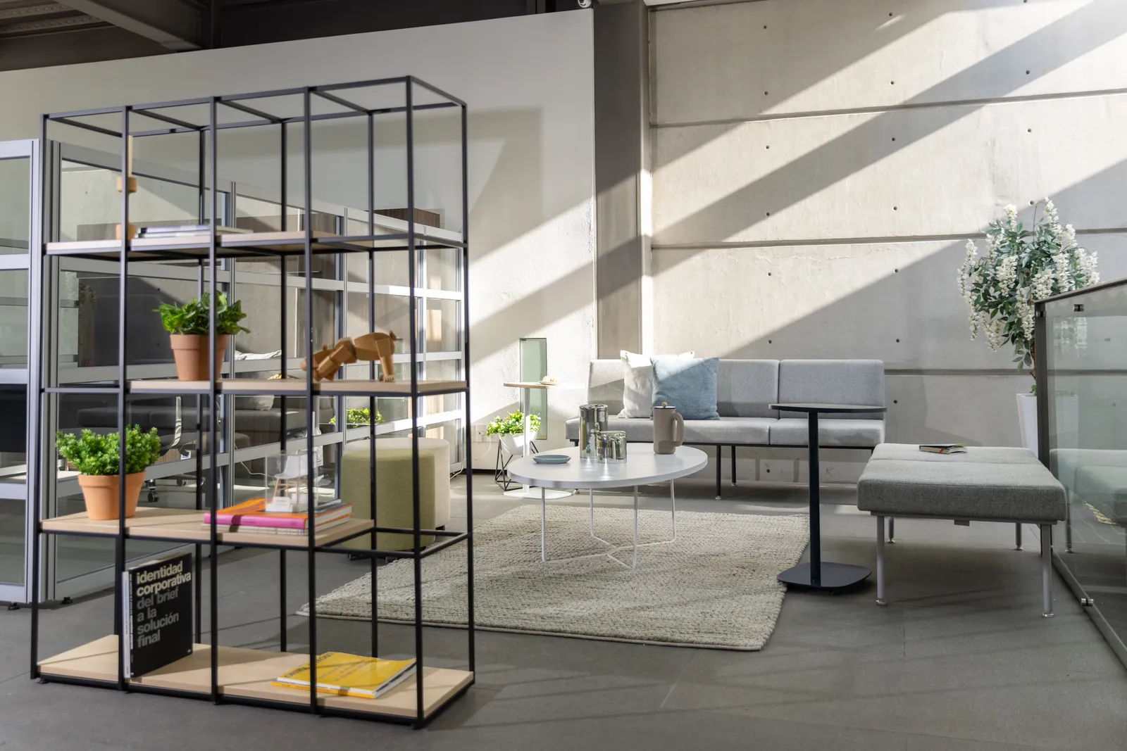 Área lounge del showroom de Poliarte con librero metálico, sofá gris, banca y mesa de centro blanca