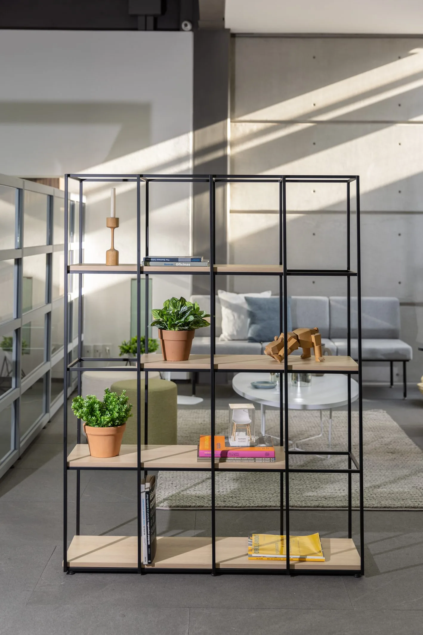 Showroom de Poliarte en Tizapán: librero metálico con plantas frente a una sala lounge