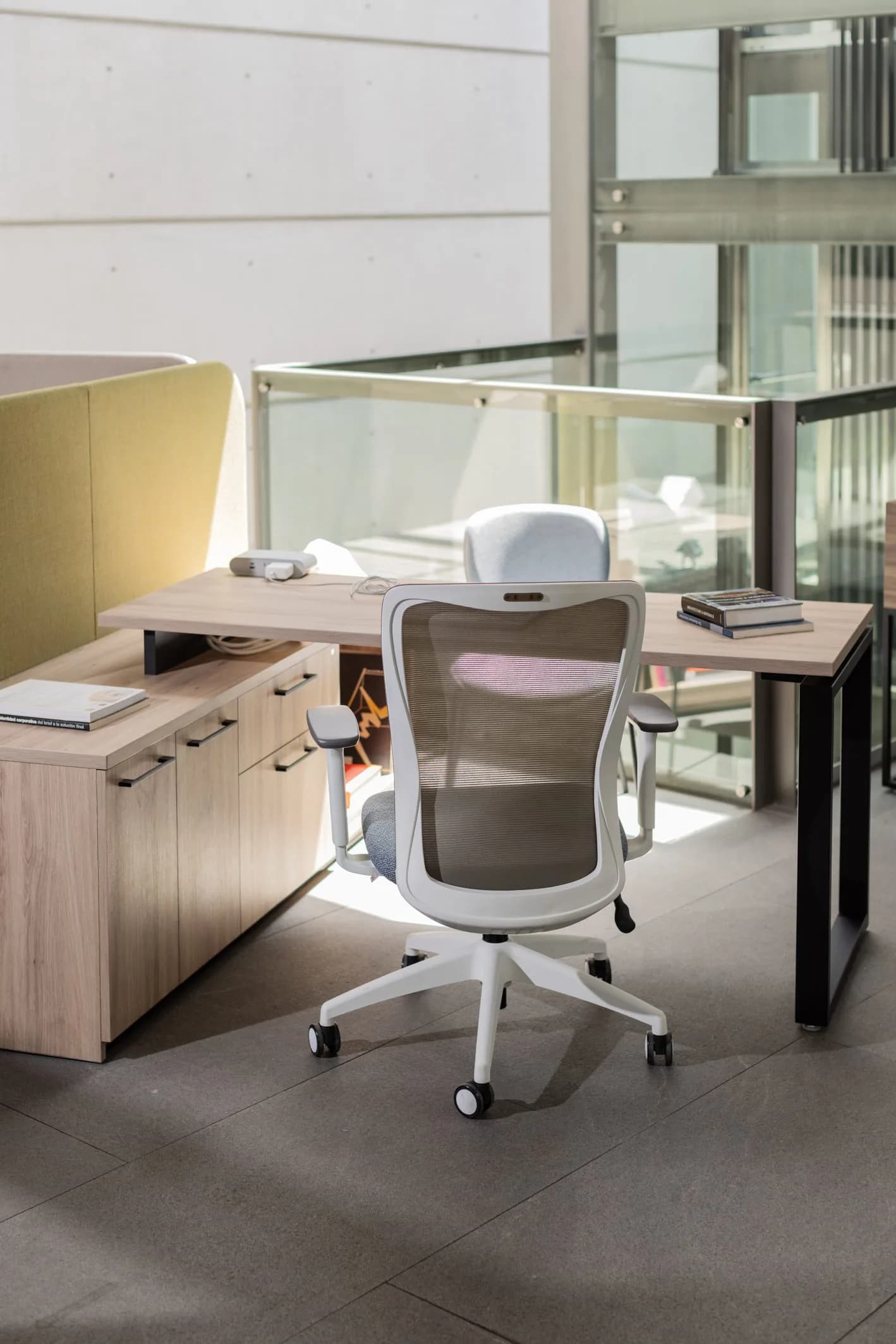 Escritorio con credenza de madera clara, panel tapizado verde y silla de malla blanca en el showroom de Poliarte