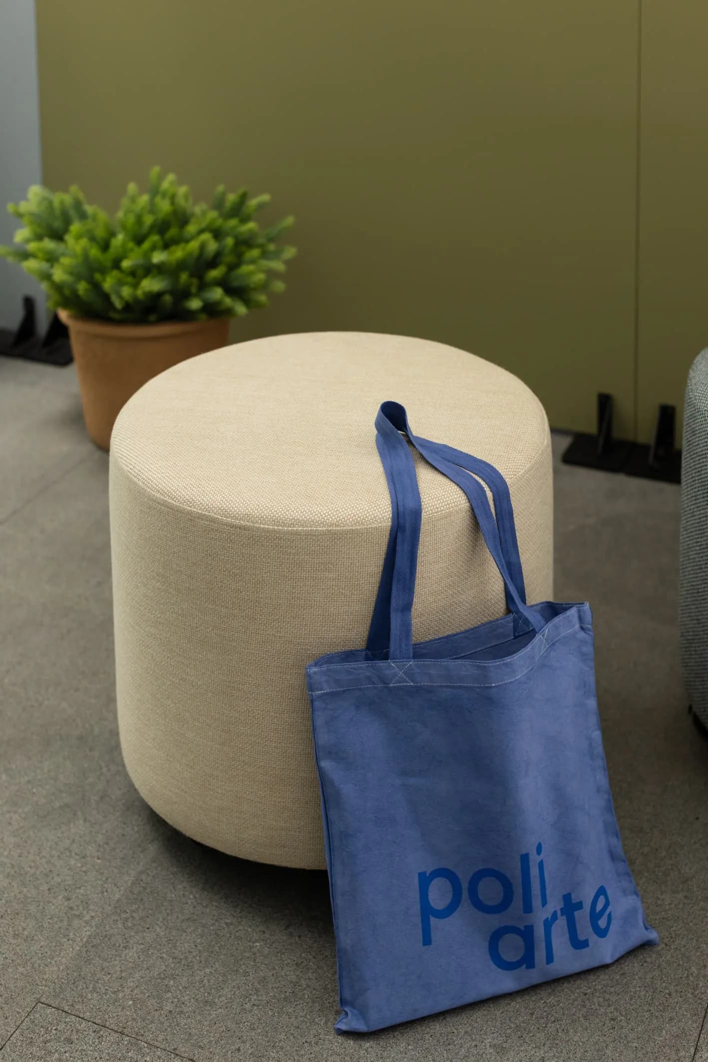 Bolsa de tela azul con el logo de Poliarte recargada en un puf beige del showroom