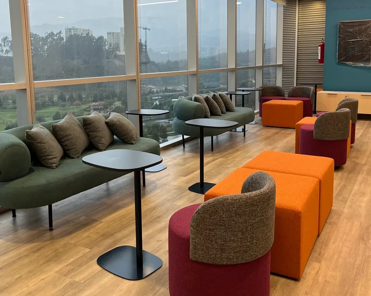 Área lounge de Viatris con sofá verde, sillones tapizados, puffs naranjas y mesas altas, por Poliarte