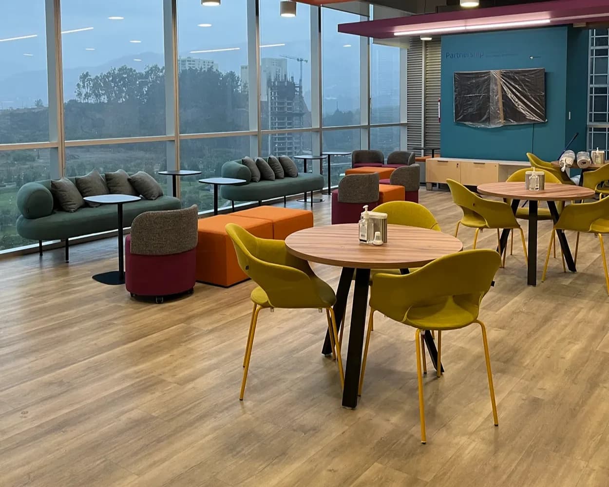 Comedor de Viatris con mesas redondas de madera, sillas amarillas y lounge al fondo, mobiliario de Poliarte