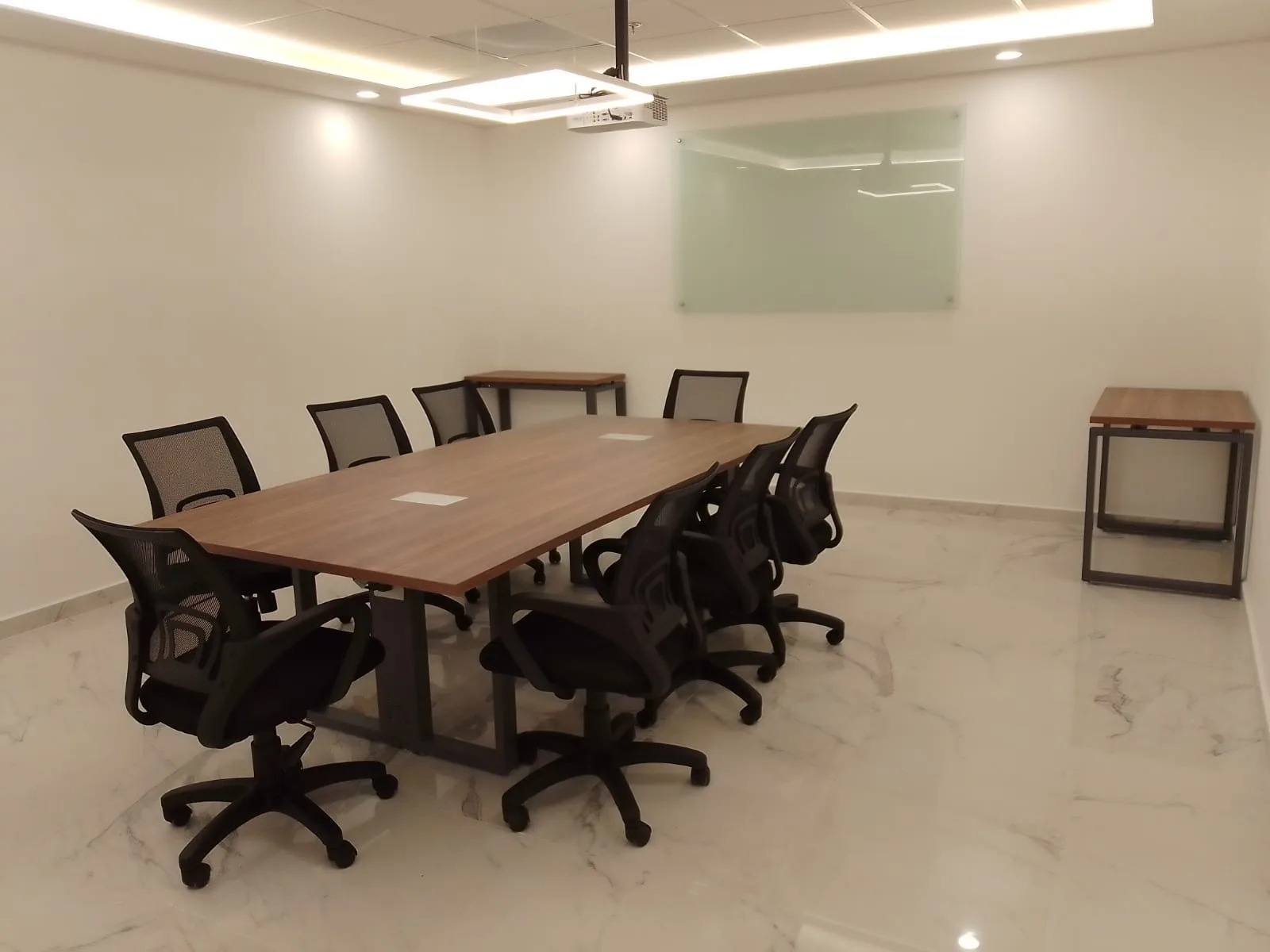 Sala de juntas de Cayeno con mesa nogal para ocho y sillas negras de malla, por Poliarte