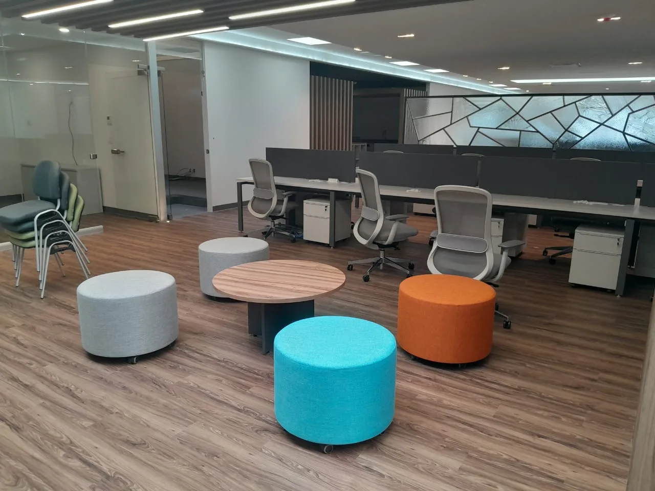Zona informal de BA Glass con puffs de colores y mesa redonda junto a estaciones, por Poliarte