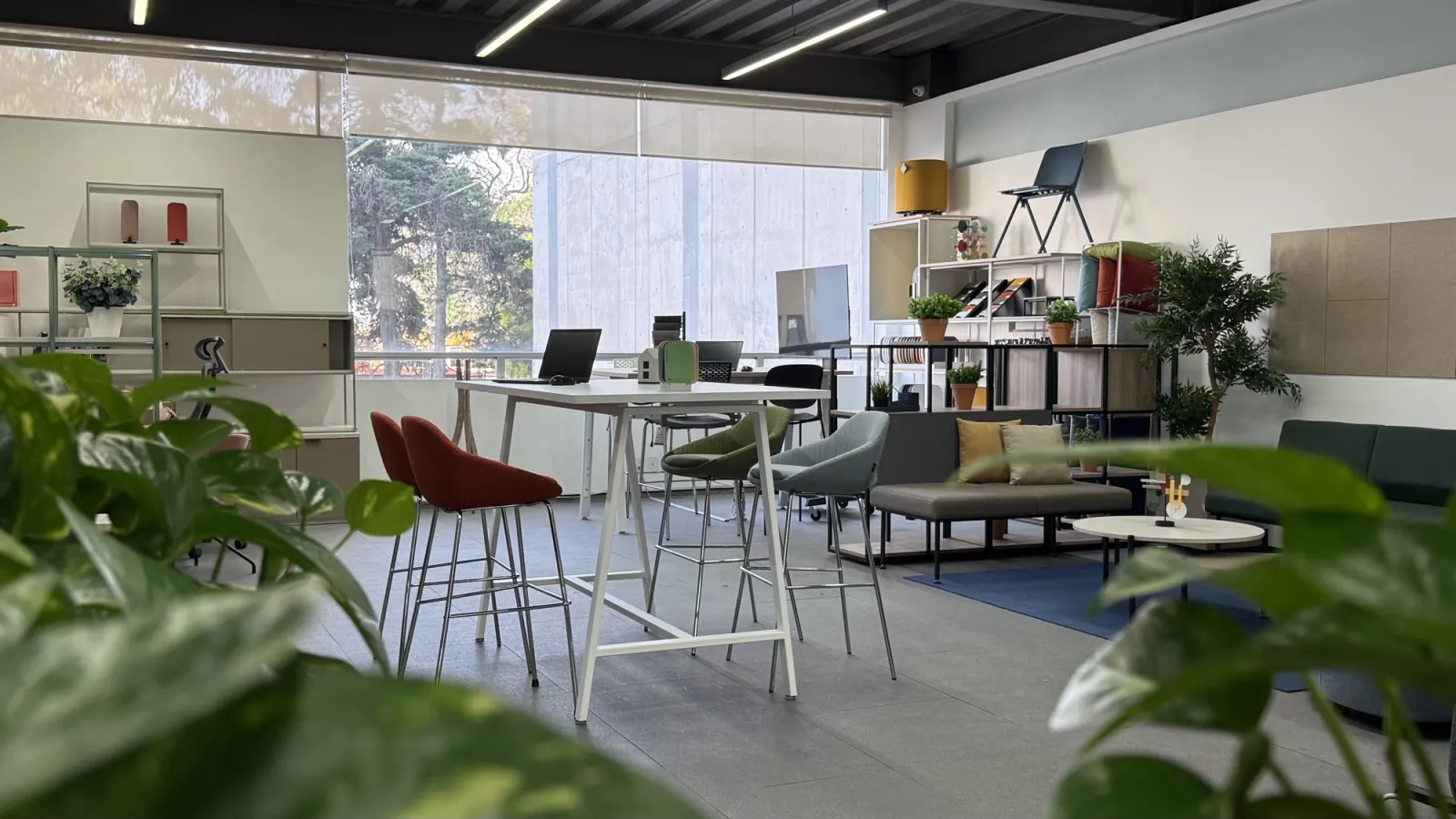 Área de colaboración en el showroom de Poliarte, con mesa alta, asientos y estanterías de materiales